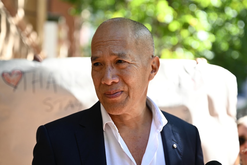 Bald man in suit in front of poster