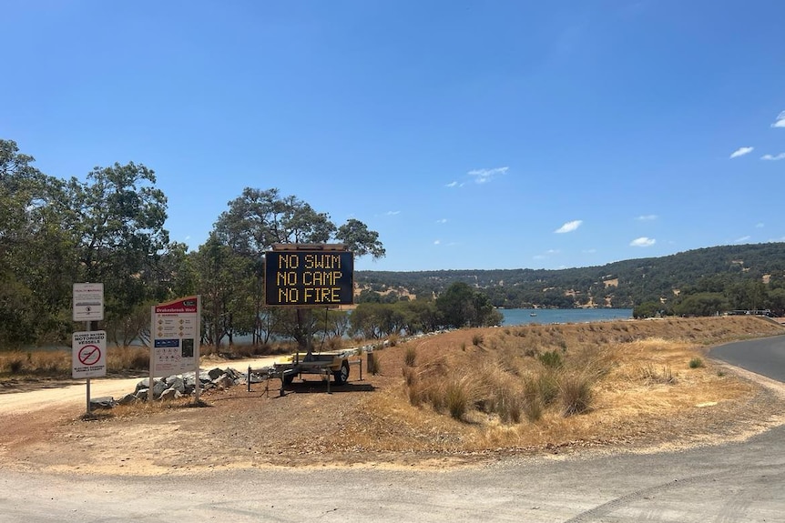 A dam with signs in front of it saying 'no swim, no camp, no fire'.