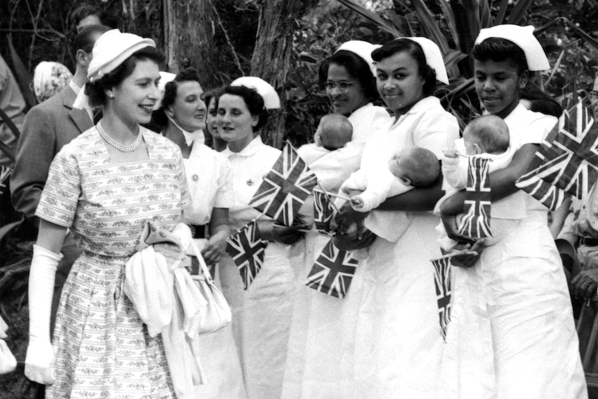 the queen beside three nurses in white uniforms, each bearing union flags and a triplet baby