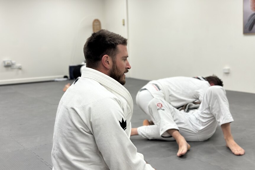 A martial arts instructor watches on as students roll in the background. 