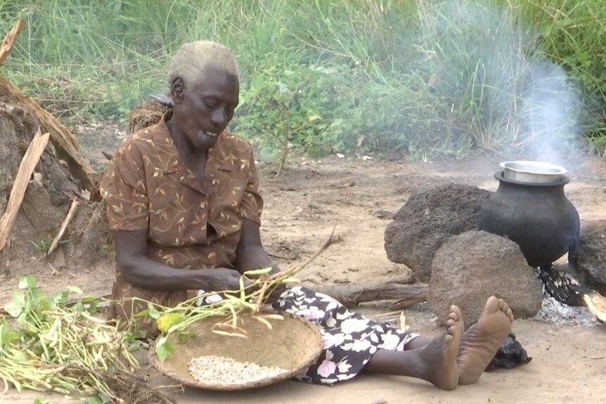 Hellen Lanyom sits on the ground, preparing food.