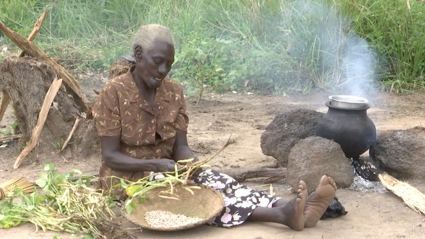 Hellen Lanyom sits on the ground, preparing food.