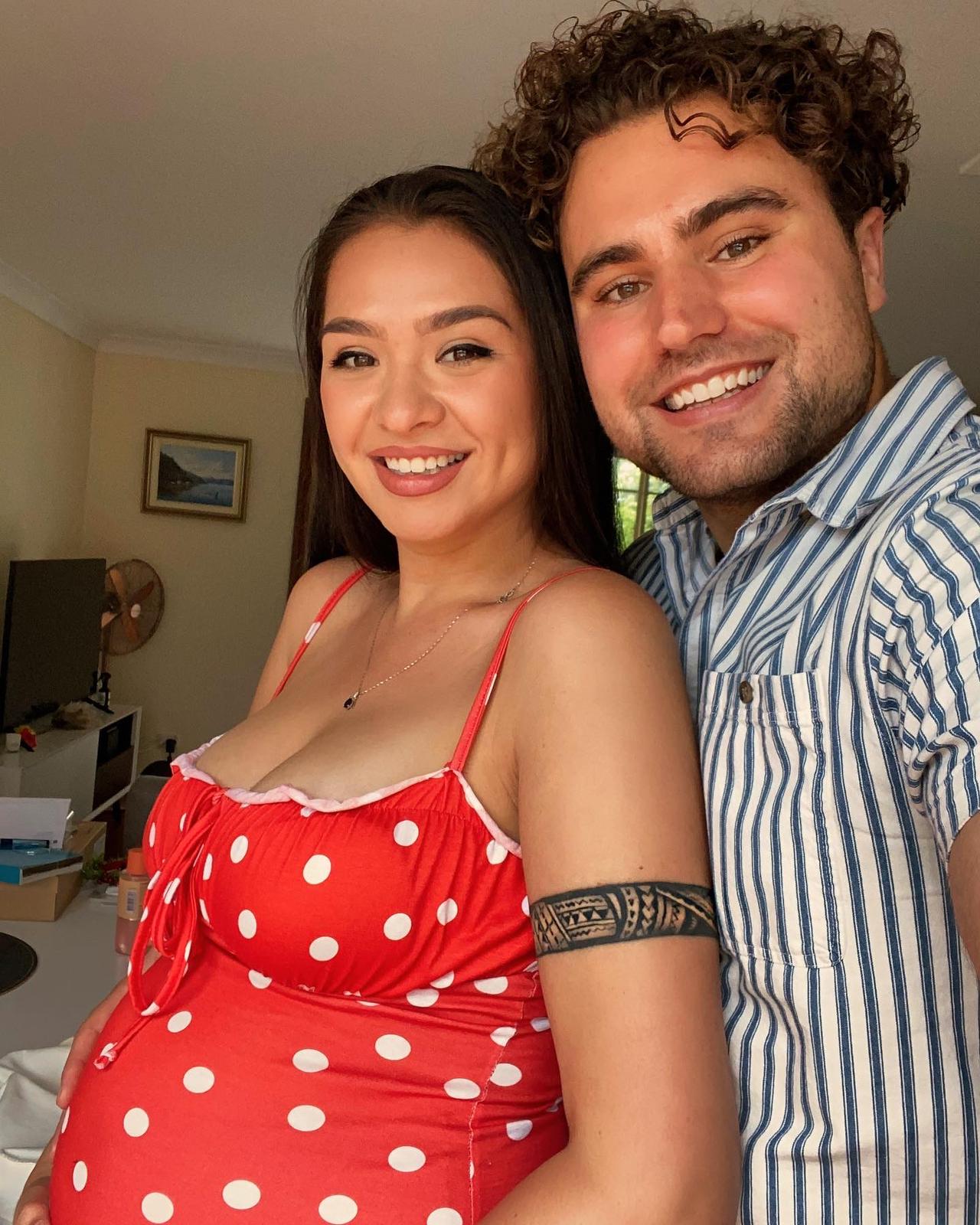 A woman wearing red polka dot dress leaning on her husband smile for selfie.