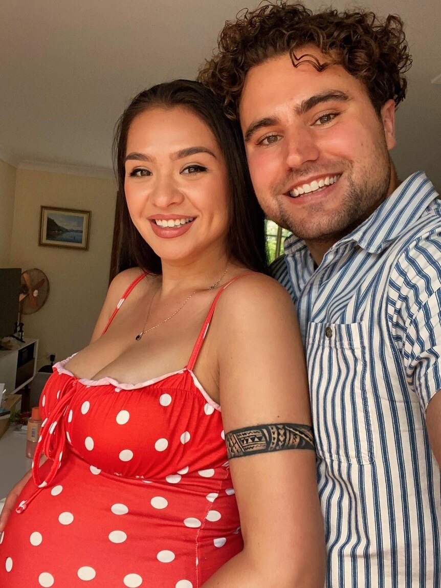 A woman wearing red polka dot dress leaning on her husband smile for selfie.