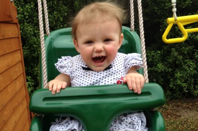 A baby girl laughs while rocking on a green plastic swing