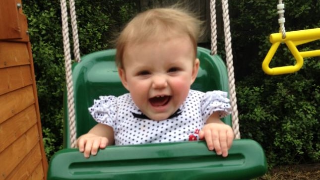 A baby girl laughs while rocking on a green plastic swing