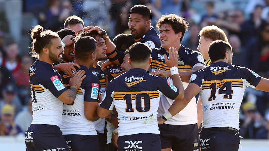 Brumbies players huddle together and rub the head of a player
