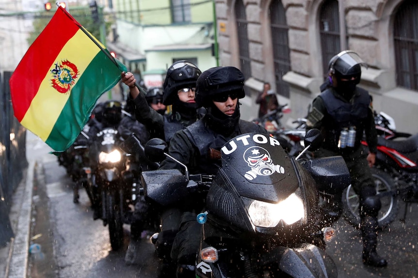 Police officers ride on motorbikes. One is waving a Bolivian flag.