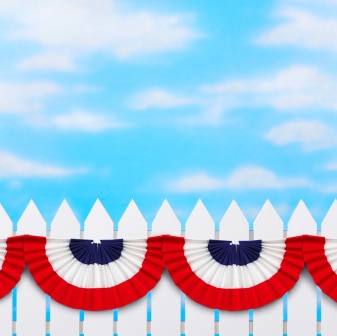 Red,white and blue bunting on a white picket fence on a blue day.