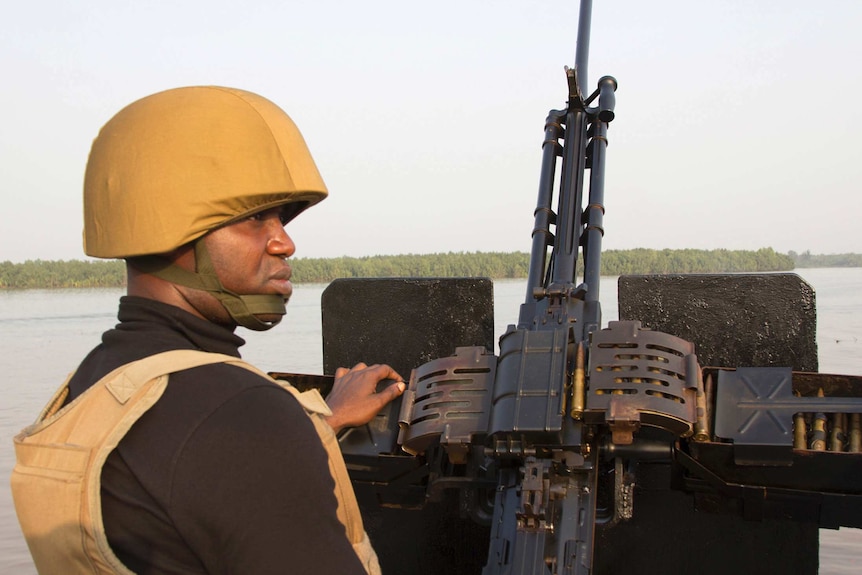 A naval officer mans a machine gun on a boat.