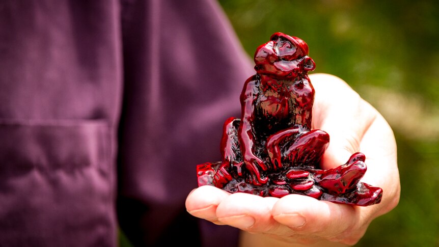Close up of a small glossy red monkey statue held on a man's palm.