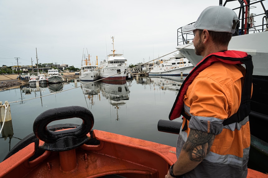 A man wearing a life vest looks across to other boats on Darwin Harbour. 