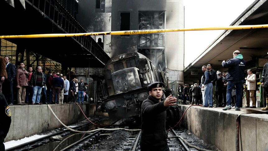 Policemen stand guard in front of a damaged and burnt out train.