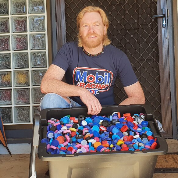 A man kneels behind a large container of plastic lids.