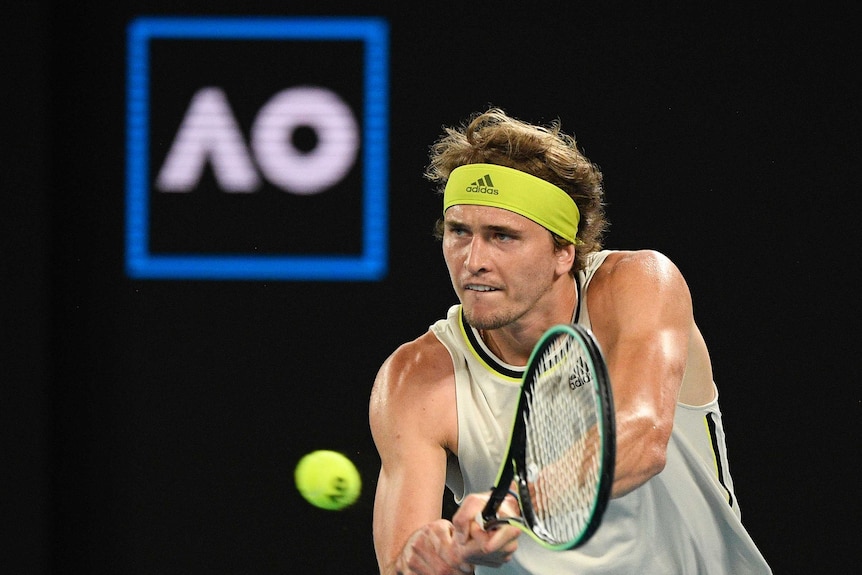 A tennis player bites his lip as he hits a backhand with an Australian Open sign in the background.