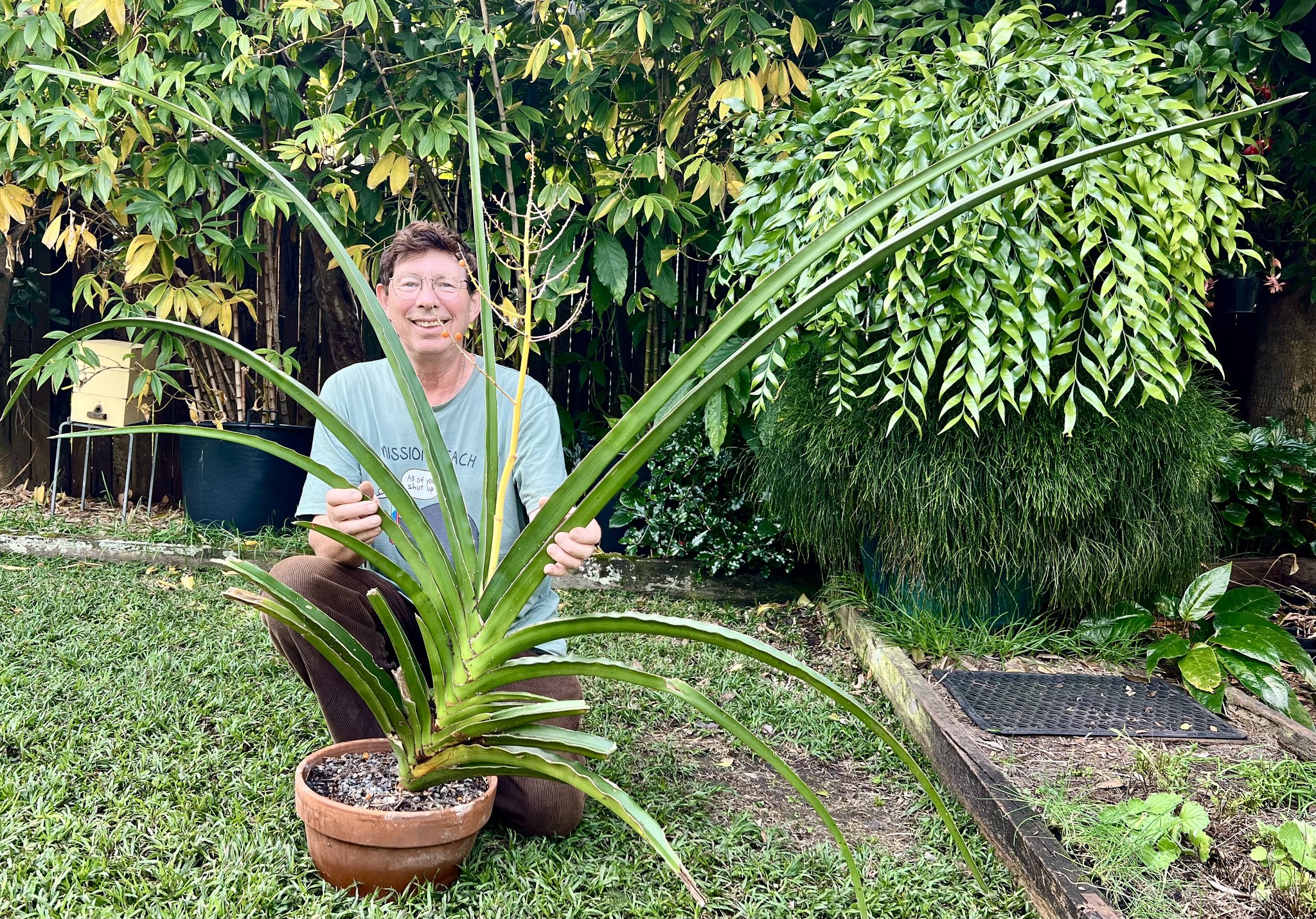 Jerry Coleby-Williams squats smiling in a backyard behind a giant potted succulent