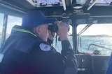A Marine Rescue officer in a boat looks out over a lake through a pair of binoculars.
