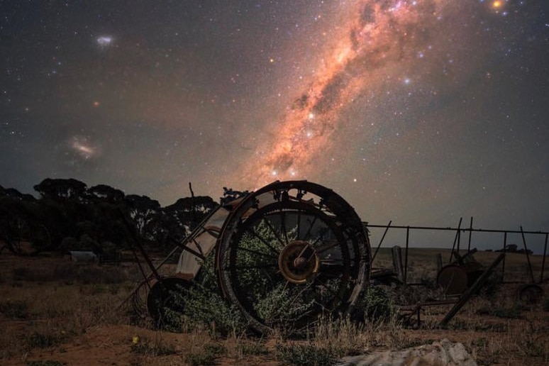 A starry sky with a pinkish collection of stars. Old metal equipment is in the foreground.