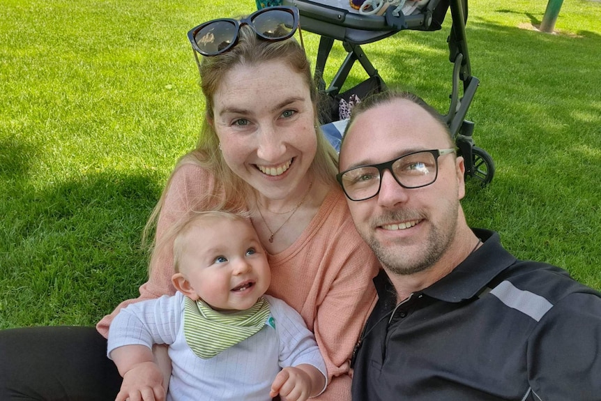 woman and man with baby smiling looking happy sitting on green grass