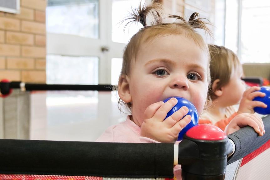 A close up shot of a baby with a ball in her mouth