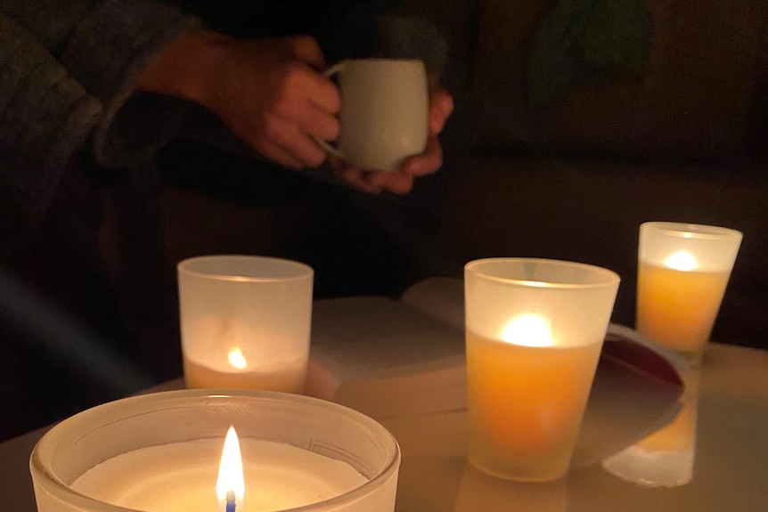 A person holds a coffee mug with lit candles on the coffee table during a blackout.