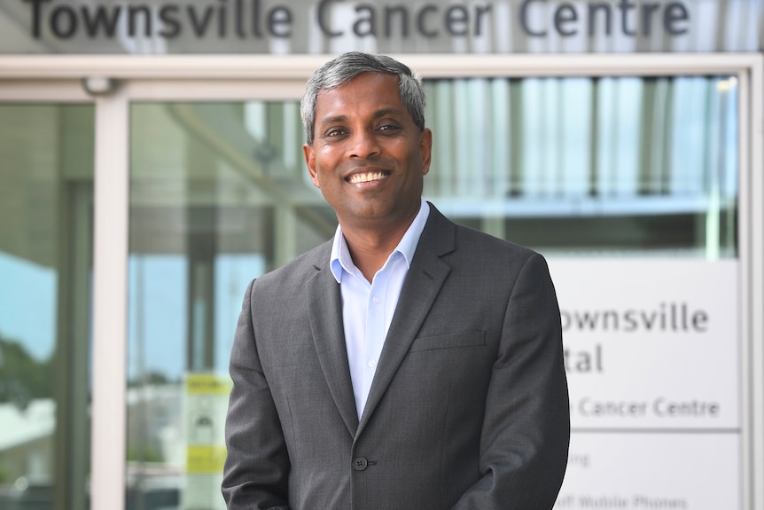 A man in a grey suit standing outside the Townsville Cancer Centre, smiling