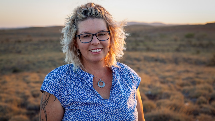 Presenter Kelly Gudgeon smiling at the camera with the sparse Pilbara landscape in the background