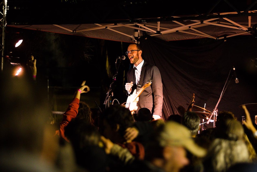 Guitarists in suit calling out to very responsive crowd at an outdoor venue at night.