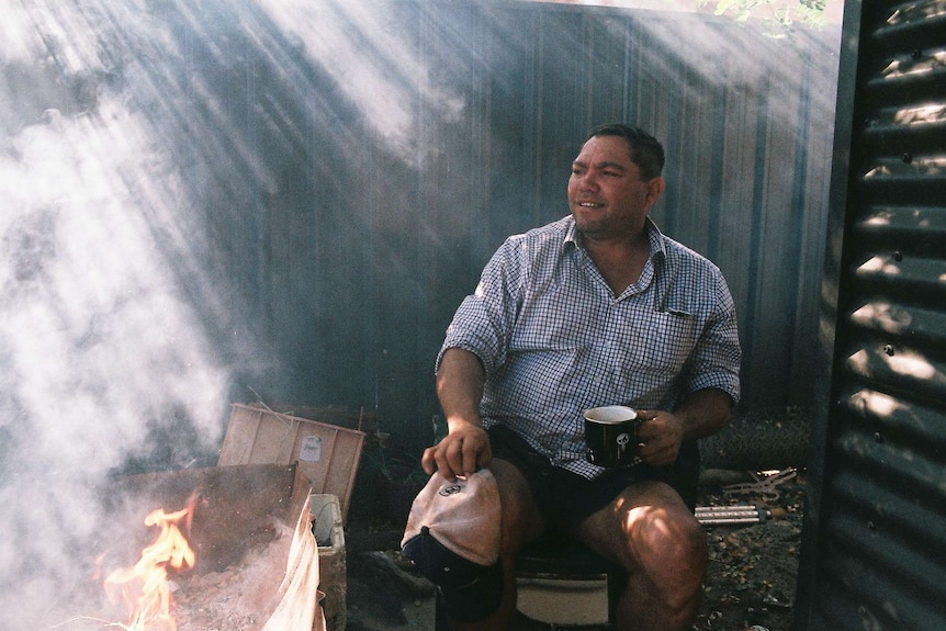 A man sits next to a camp fire.