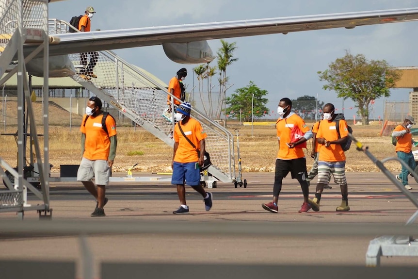 Workers wearing face masks disembark from a plane and walk across the tarmac.