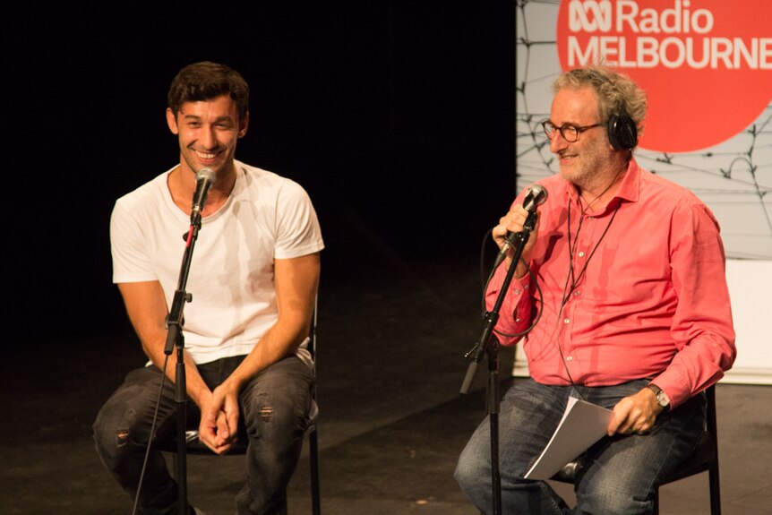 Two men sit on stools behind microphones, banner in background reads 'ABC Radio Melbourne'.