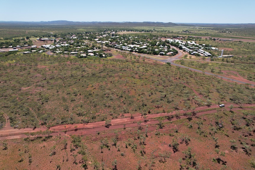 A drone shot of a red rural outback setting with a town settlement in the background