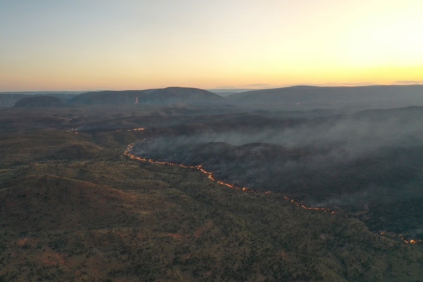 a fire burning through an arid and hilly landscape.