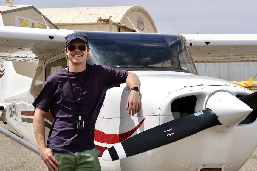 A man stands next to a small plane. He is smiling.