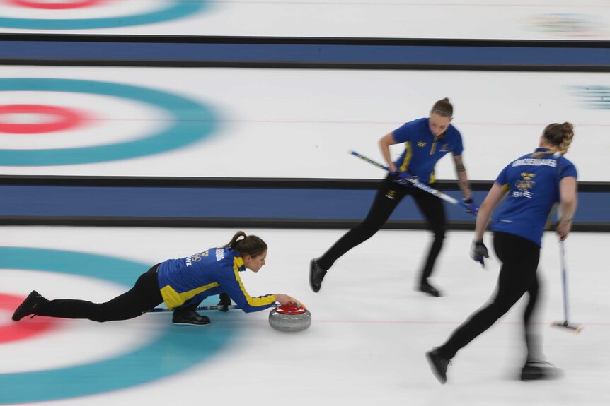 Swedish curler releases the stone as two teammates stand alongside.