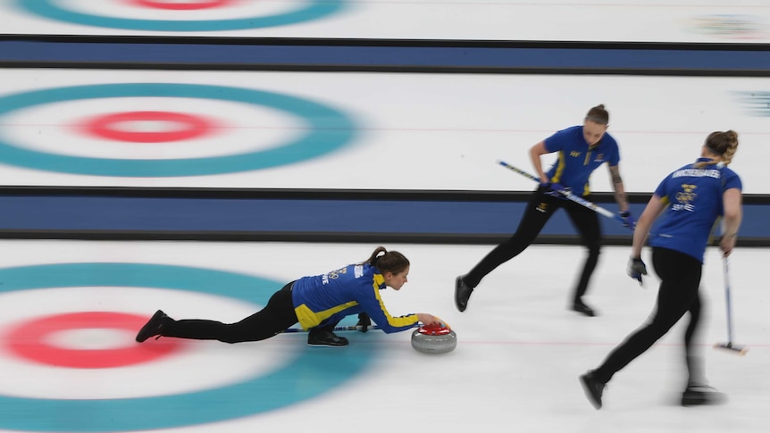 Swedish curler releases the stone as two teammates stand alongside.