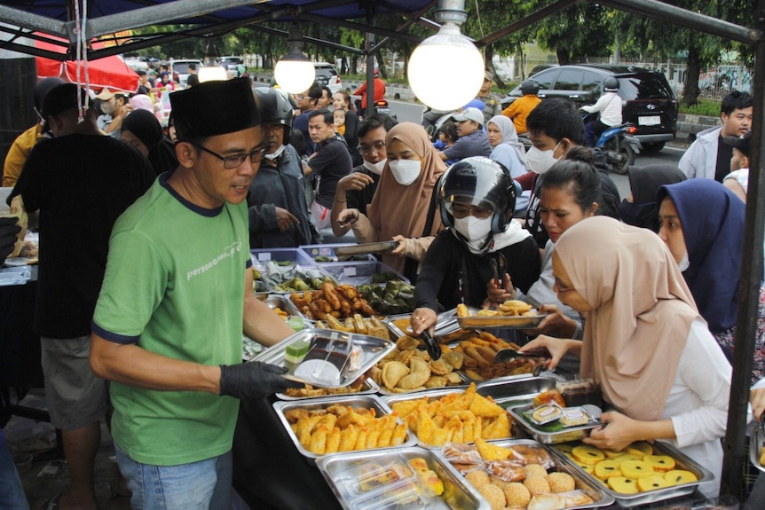 A male seller surrounded by customers wearing hijab.