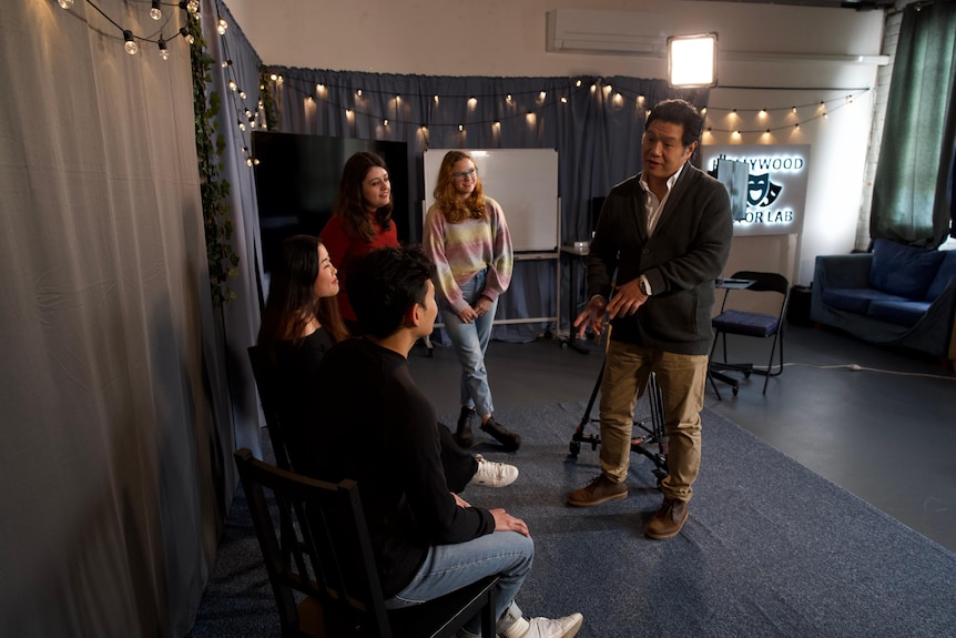 Four students in a drama class with an Asian male teacher. 