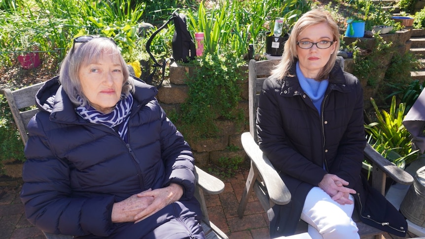 Two women, who are sitting outside, look at the camera