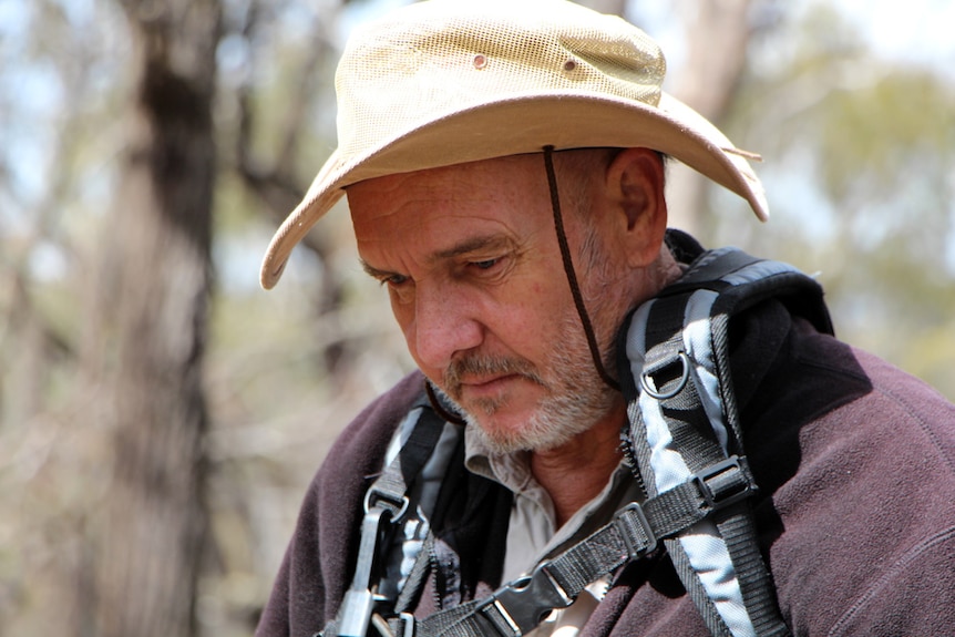 A man with a broadbrim hat mining for gold with a metal detector