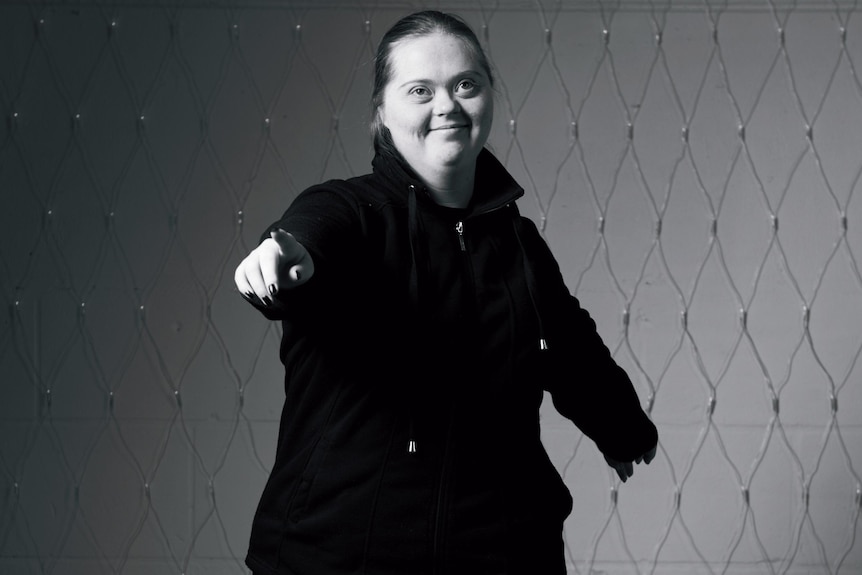 A portrait of a woman smiling at camera in a black polar-fleece jacket. She has an intellectual disability.