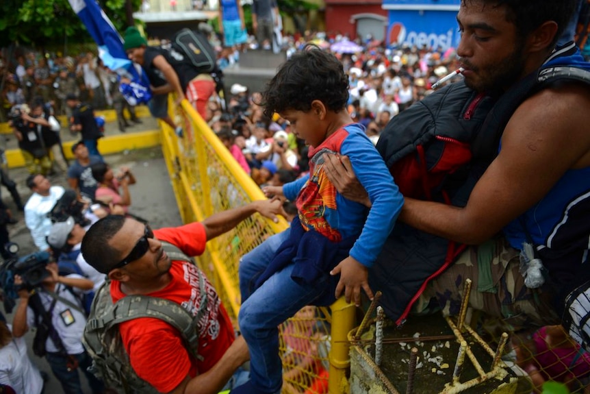 A child is passed over a border fence between Guatemala and Mexico.