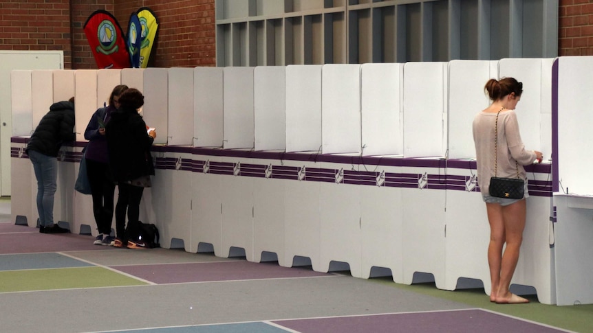 Four voters stand in an otherwise empty line of polling booths.