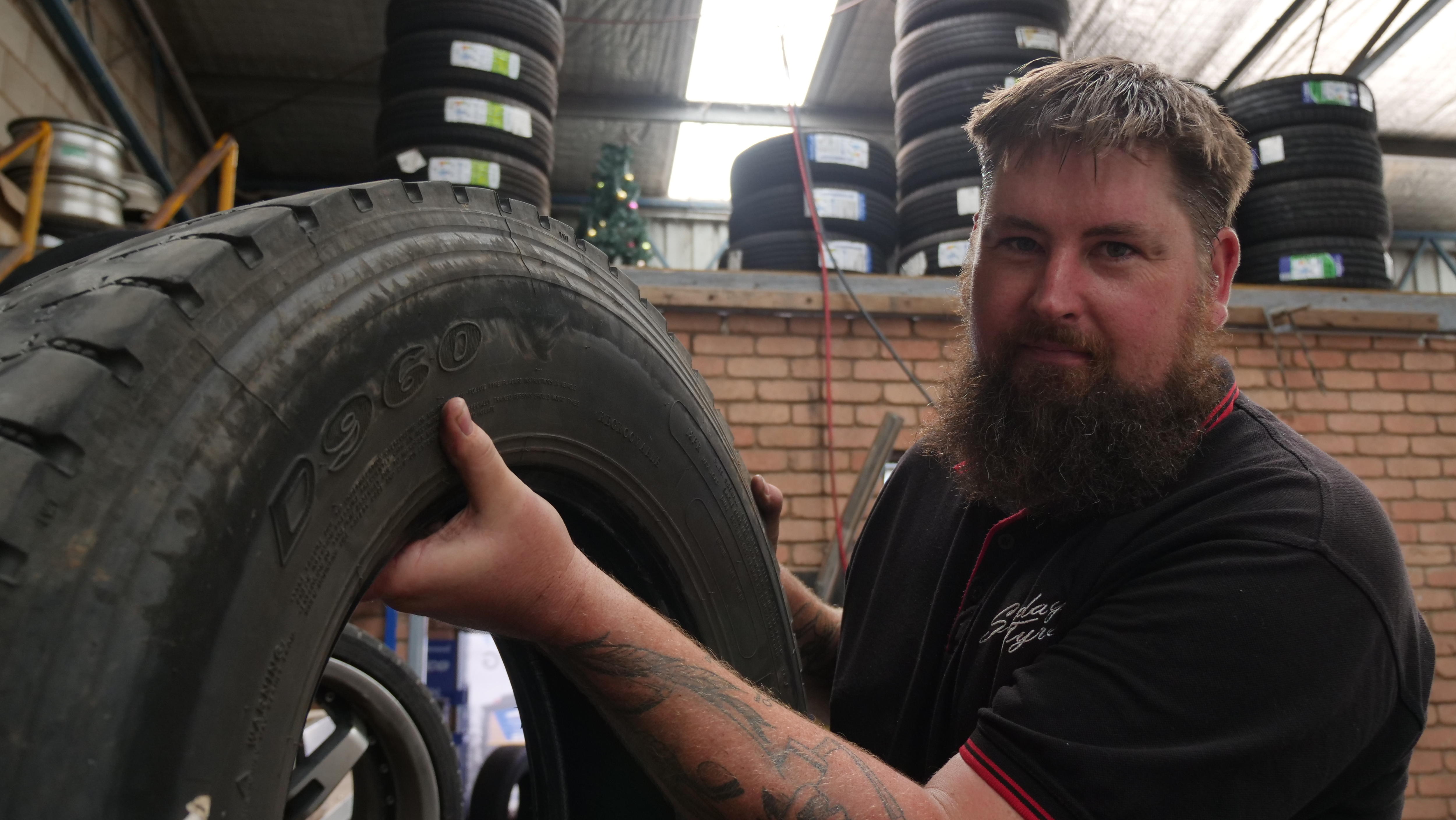 A man holds a tyre in a tyre shop. 
