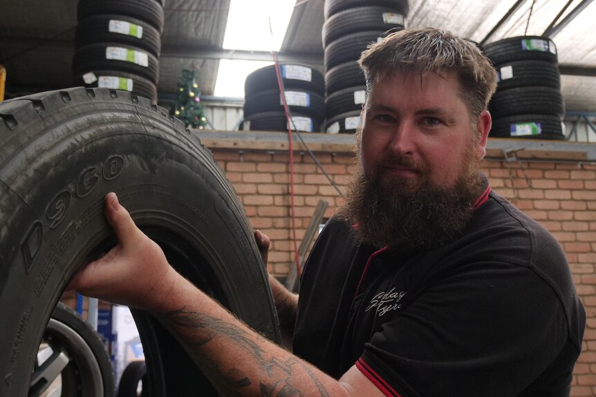 A man holds a tyre in a tyre shop. 