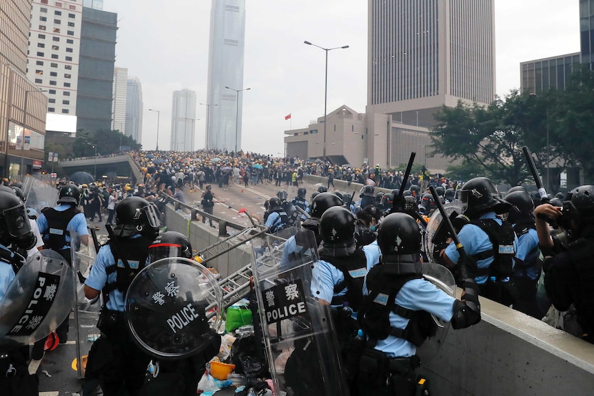 Looking down a raised expressway, Hong Kong police present a blockage to hundreds of protesters gathered further up the road.