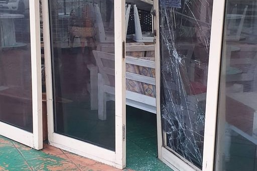 Glass doors are ajar, with a large glass smash on the bottom of one window, glass pieces are all over the floor.
