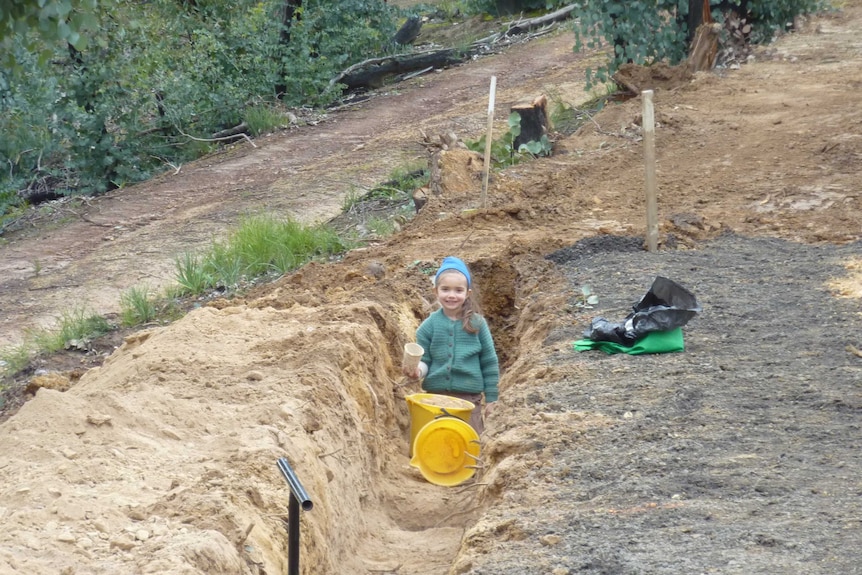 A young girl in a trench with a bucket