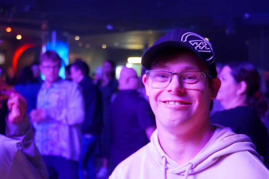 A young man in a baseball cap smiles in a nightclub.