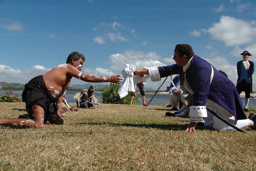An Aboriginal man and man dressed as 18th century British marine both kneeling with arm outstretched towards each other